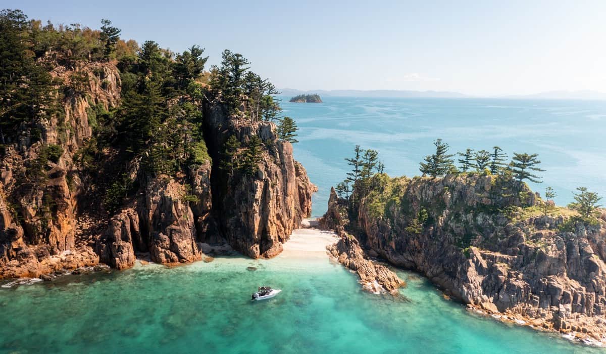 Aerial view of a secluded tropical beach and rocky island surrounded by clear turquoise water in the Whitsundays